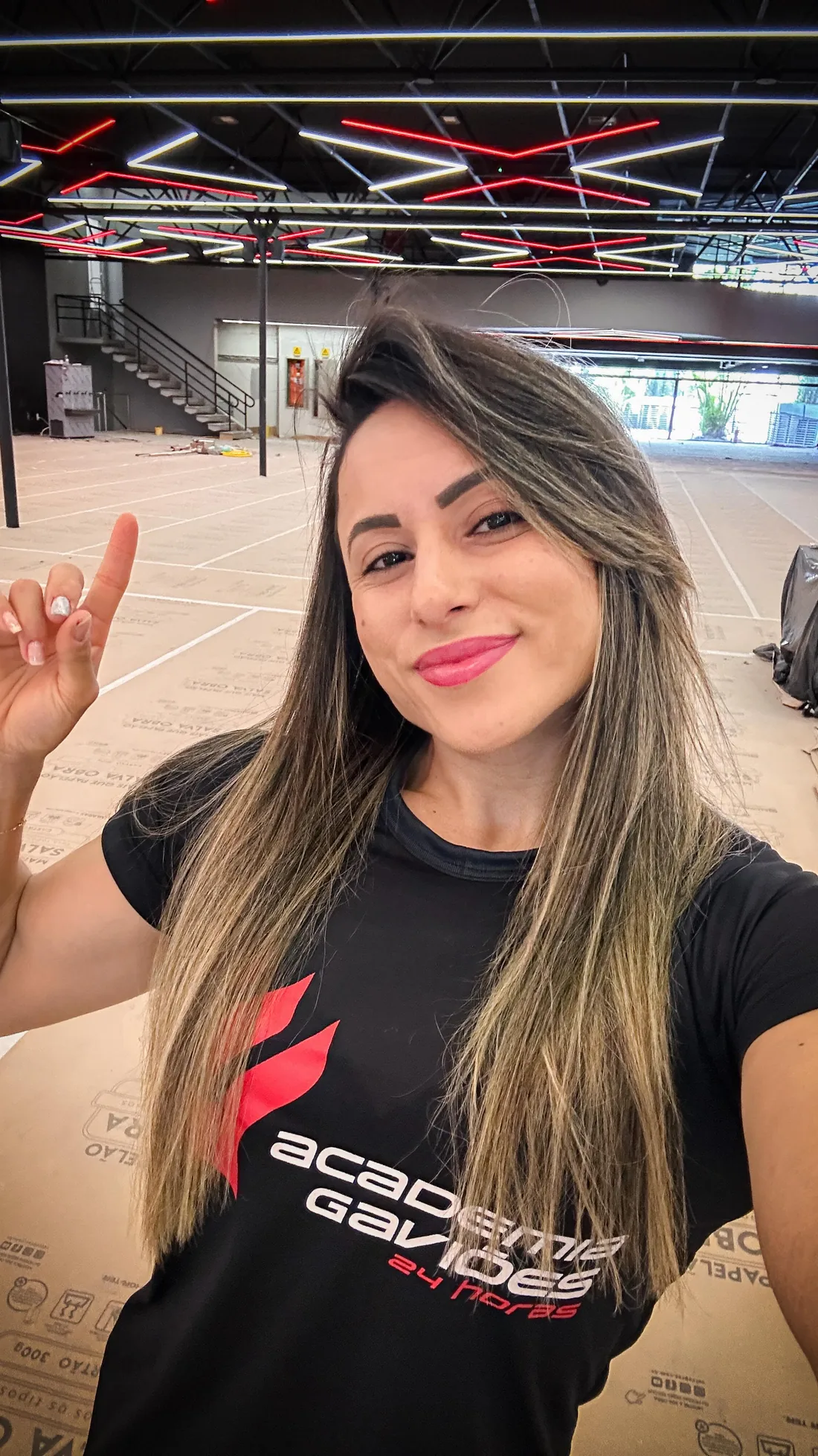 Monique Ribeiro de camiseta preta da Academia Gaviões apontando para cima na unidade ainda em montagem