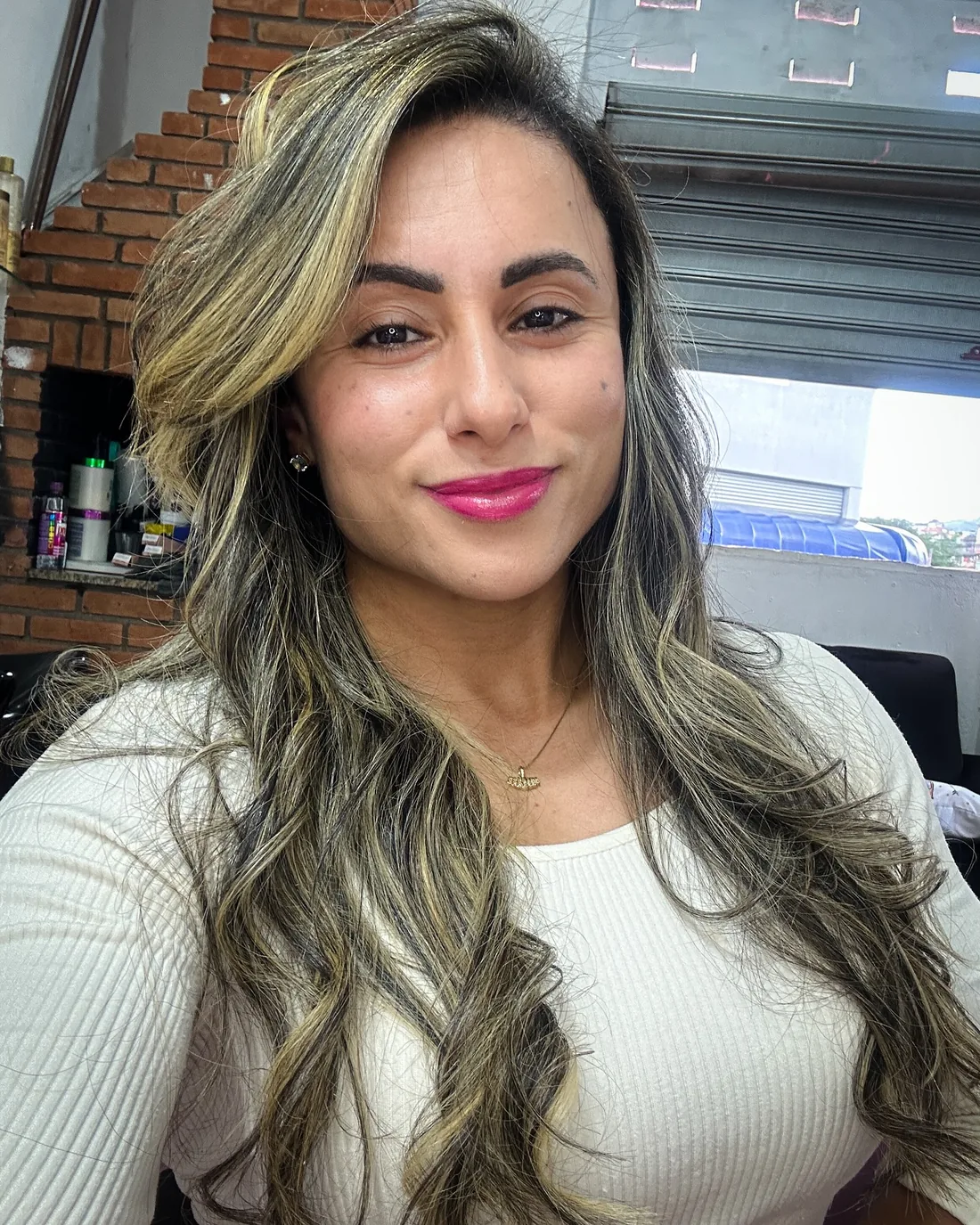 Retrato de Monique Ribeiro com cabelo longo iluminado e blusa branca, sorrindo de leve