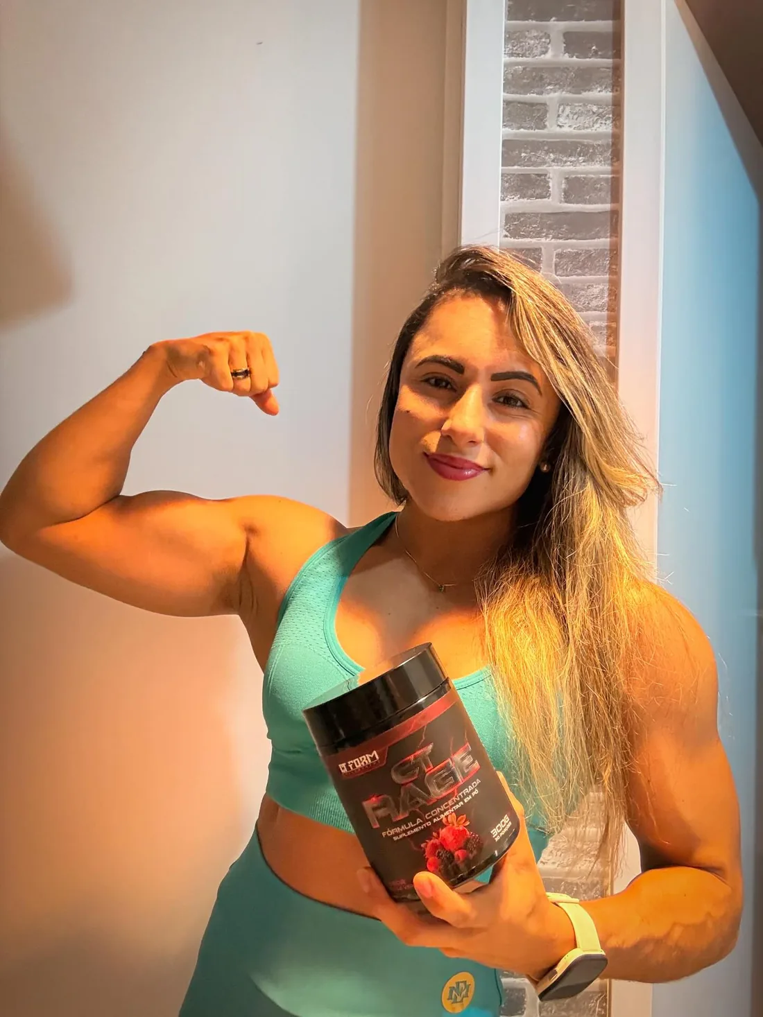 Monique Ribeiro flexionando o bíceps e segurando o pré-treino da CT Form Suplementos