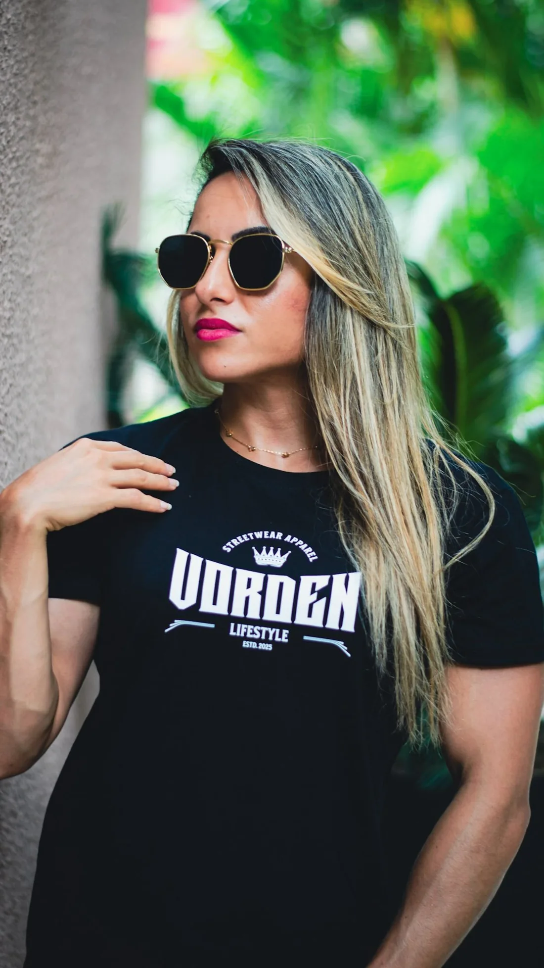 Monique Ribeiro de óculos escuros e camiseta preta Vorden Lifestyle entre plantas