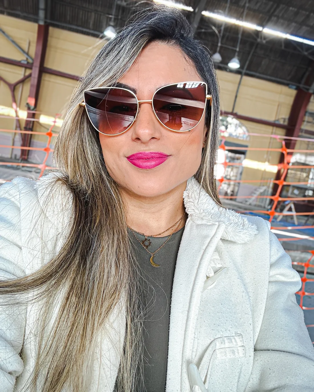 Monique Ribeiro de óculos escuros gatinho e casaco branco sorrindo em selfie