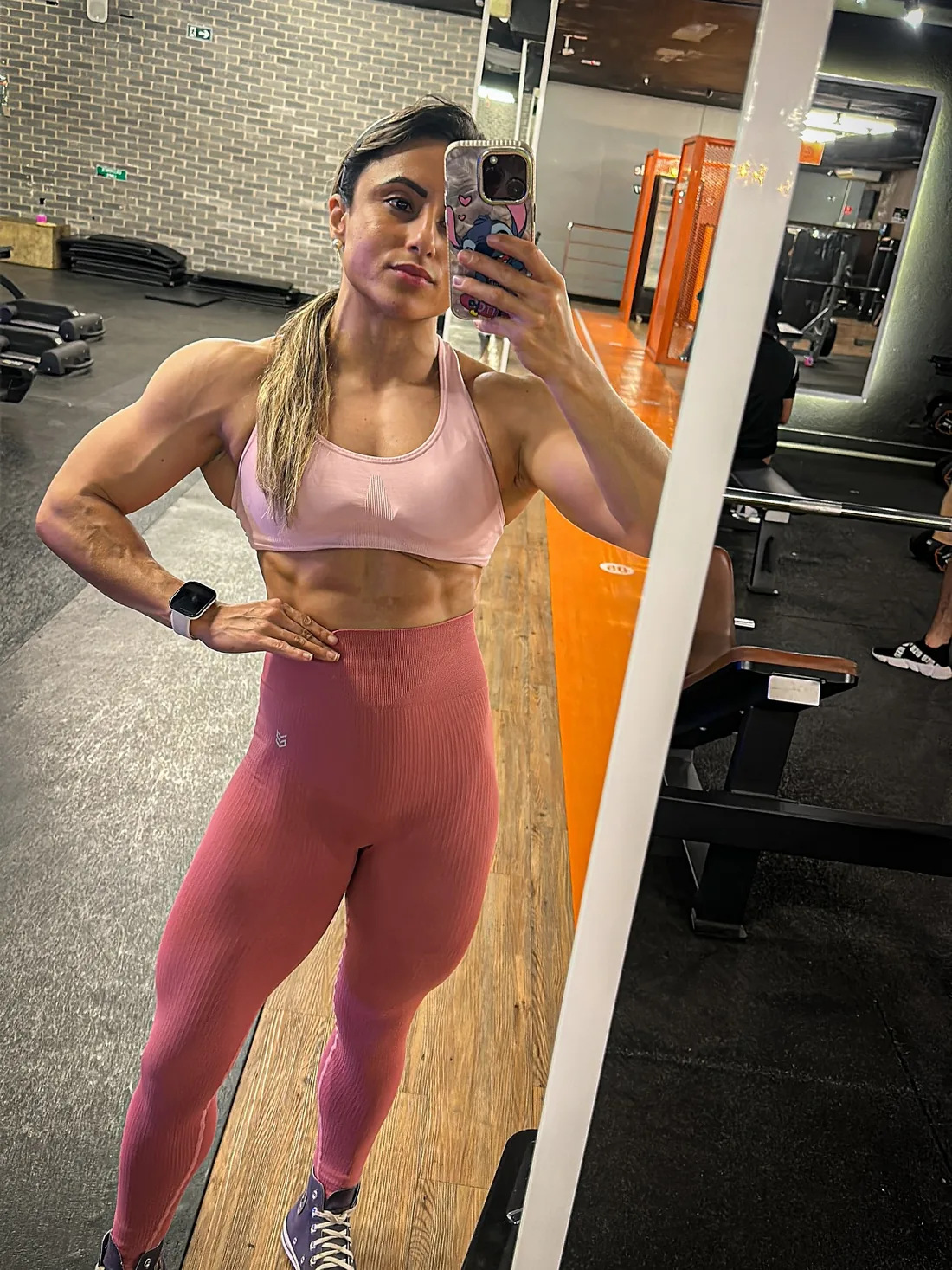 Monique Ribeiro de top rosa claro e legging rosa com as mãos na cintura em selfie de espelho