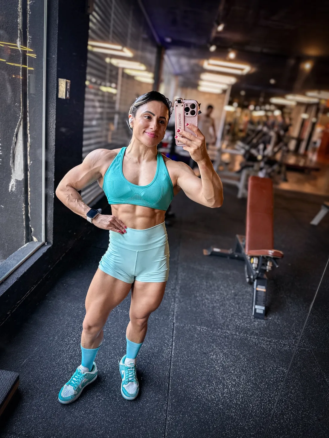 Monique Ribeiro de conjunto turquesa mostrando o abdômen definido em selfie na academia